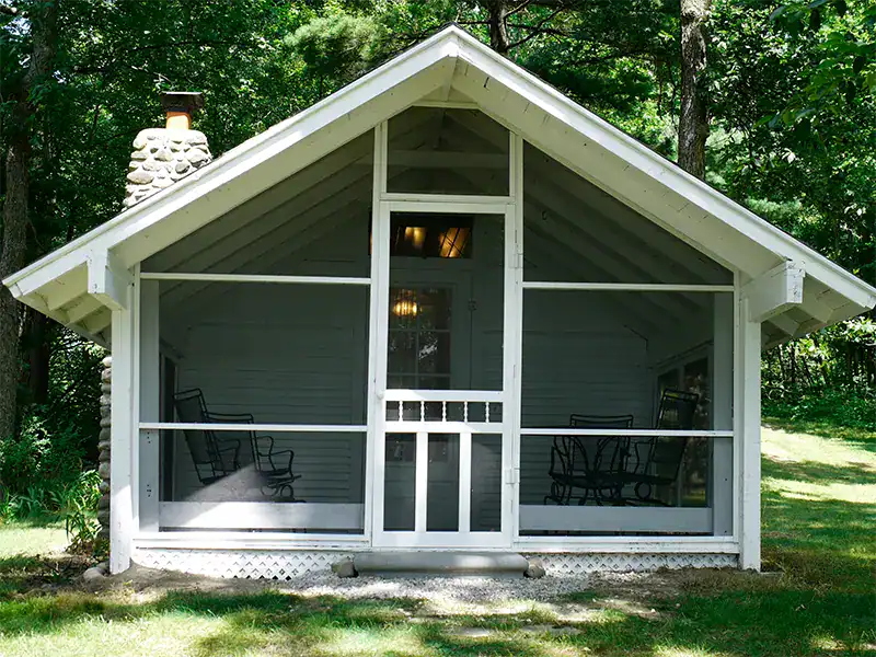 Charming screened porch cabin at Waldenwoods Resort surrounded by lush trees. Perfect for family retreats.