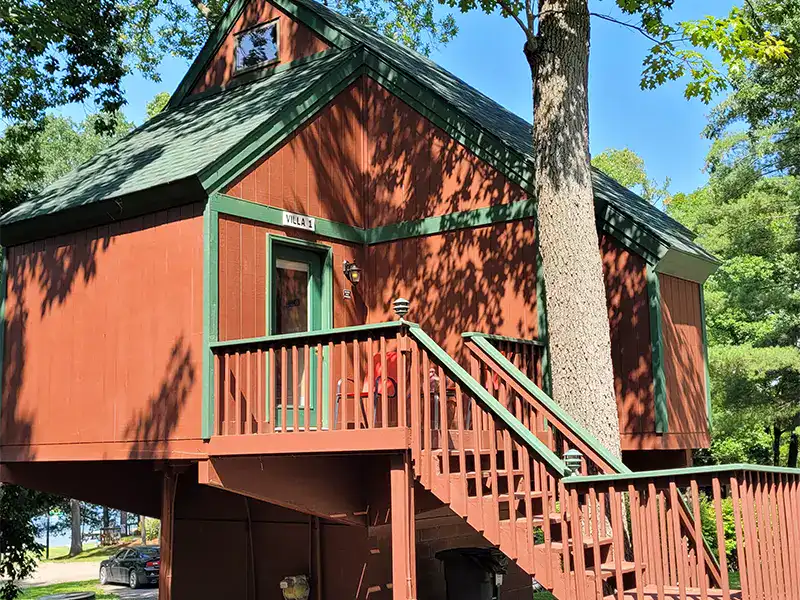Charming red cabin with green trim at Waldenwoods Family Recreation Resort, surrounded by lush trees.