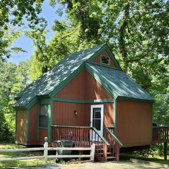Charming lakeside cabin at Waldenwoods Family Recreation Resort surrounded by lush green trees.
