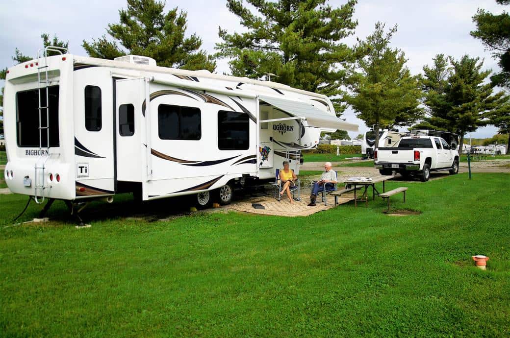 Lush green park with RVs and people relaxing, surrounded by trees and open spaces.